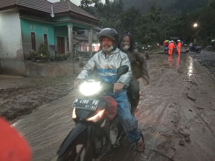 People are fleeing by motorbike.  The road is completely covered with volcanic ash.