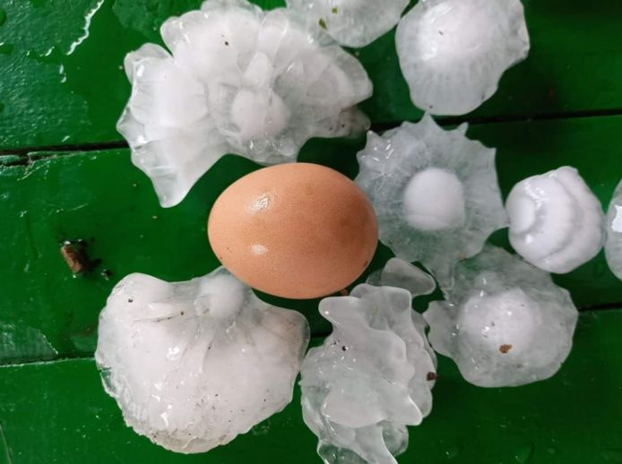 On a table beside an egg, there are several balls of hail in different shapes.
